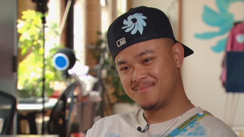 a man stares directly at the camera, wearing a backwards baseball hat