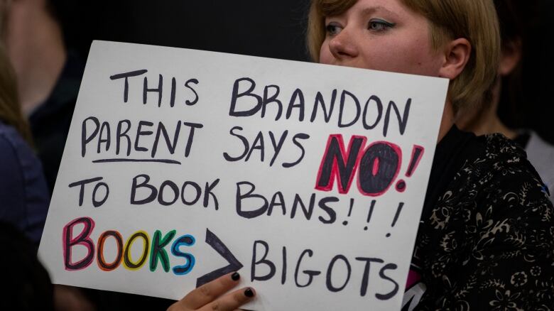 A woman holds a colourful sign against a book ban.