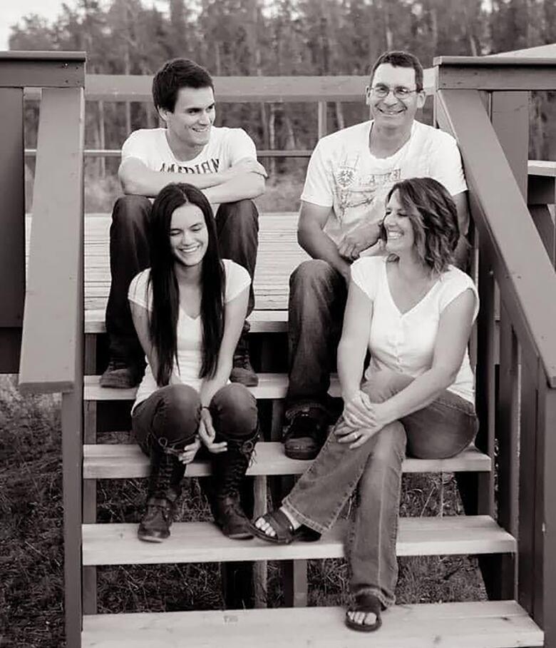 A black and white picture of four people posing as a group on some steps.