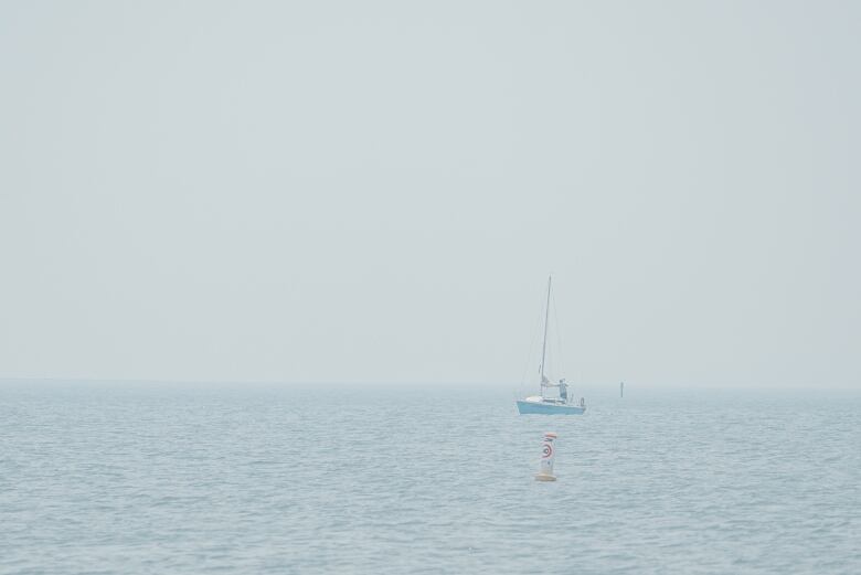 A sailboat is in the water, it's hazy due to smoke. 