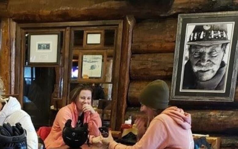 People wearing ski outfits sit in a wood panelled pub. 