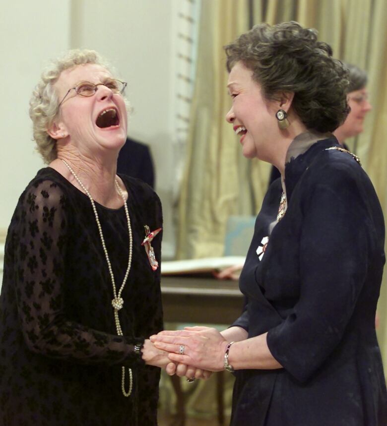 Canada's smiling governor general holds sex educator Sue Johanson's hands in hers. Johanson rocking short curly hair, glasses and a long string of pearls  throws her hair back, her mouth wide open in a joyful expression of laughter. 