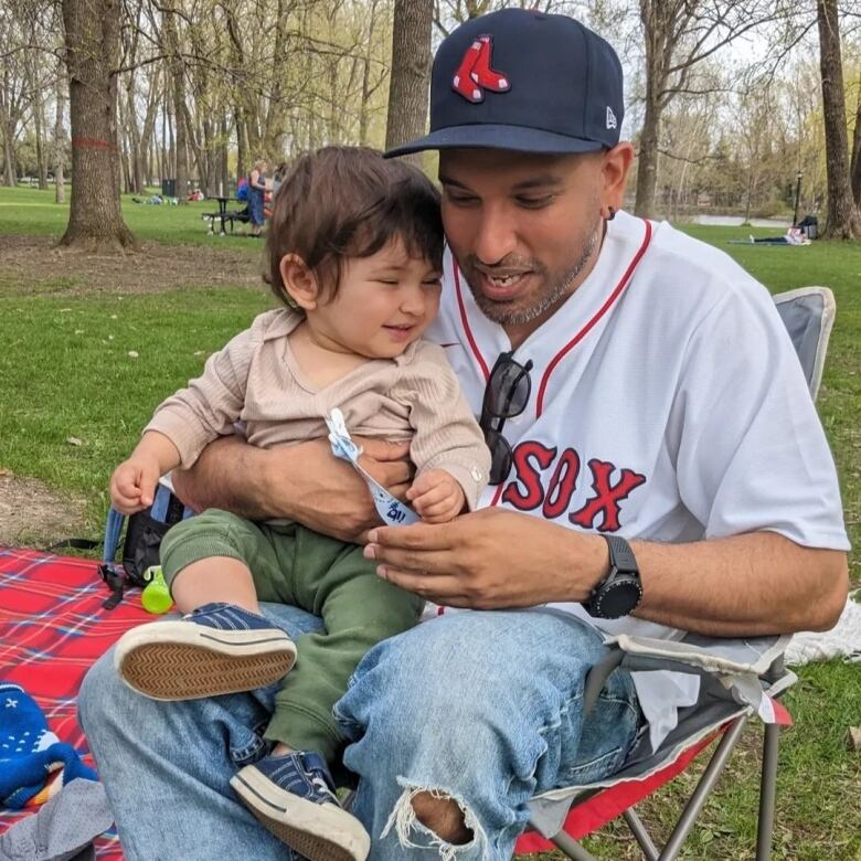 A man pictured sitting outdoors with his young son in his lap. 