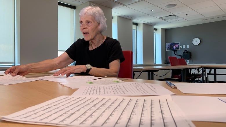 A woman sits at a desk, with sheets of paper containing handwriting in the foreground.