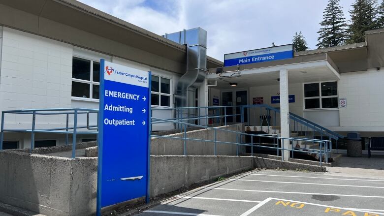 A small L-shaped bungalow with a blue Fraser Health standalone sign that says EMERGENCY, Admitting and Outpatient leads to an entrance above which reads: Main Entrance.