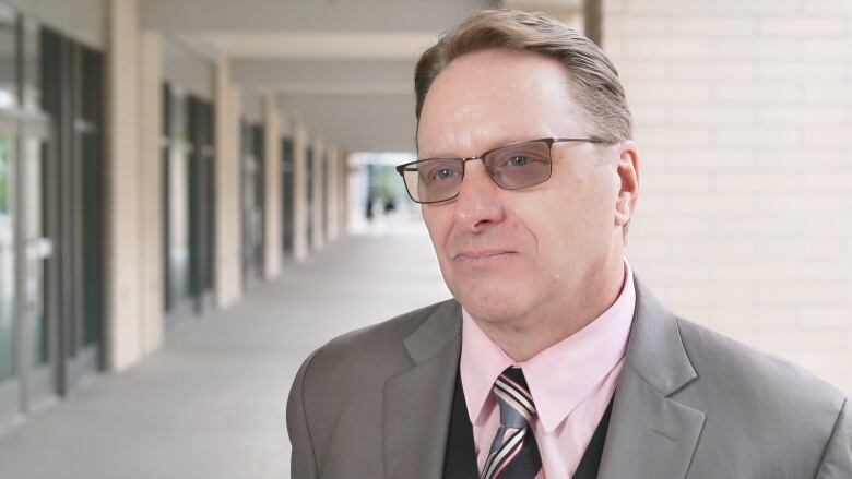 Close-up of a man wearing a suit and a pink shirt with dark glasses.