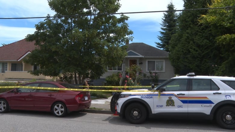 A police SUV sits outside a home with a tree and police tape surrounding it.