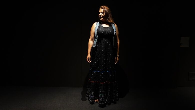 A woman stands under a spotlight on a stage in front of a black curtain.