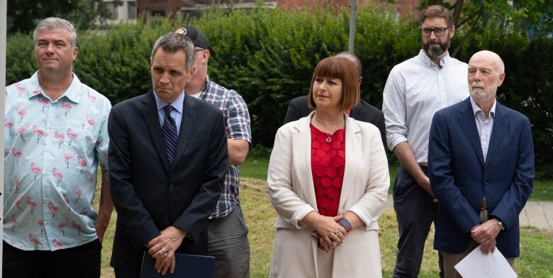 Several people stand outside on a lawn, all looking to the side