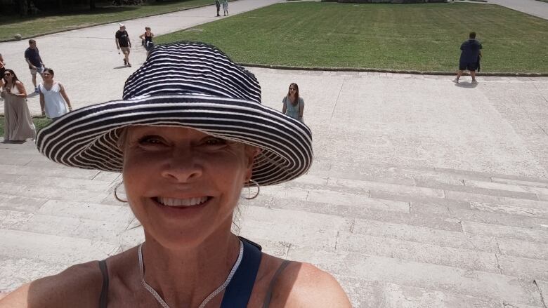 Woman in wide-brim hat stands in front of expansive palace garden.