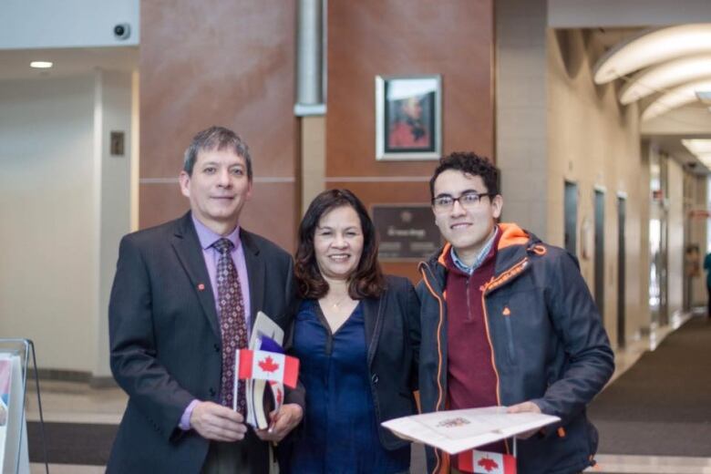 Three people stand together holding a document and a small Canadian flag. 