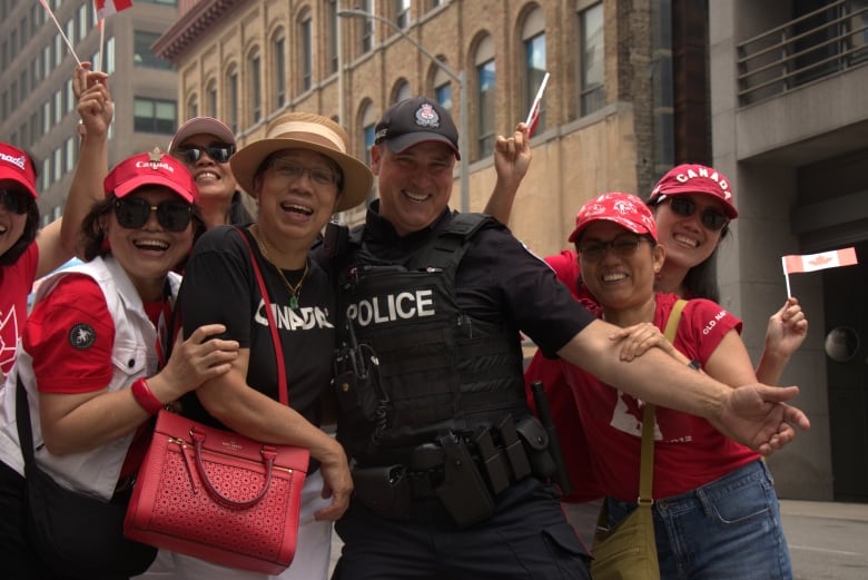 A police office poses with people dressed in red and white shits and caps.