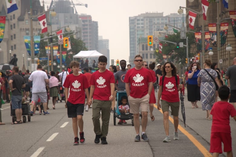 People walk down a street dressed in red and white Canada shirts.