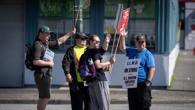 A group of men holding placards wave at a location off-camera.