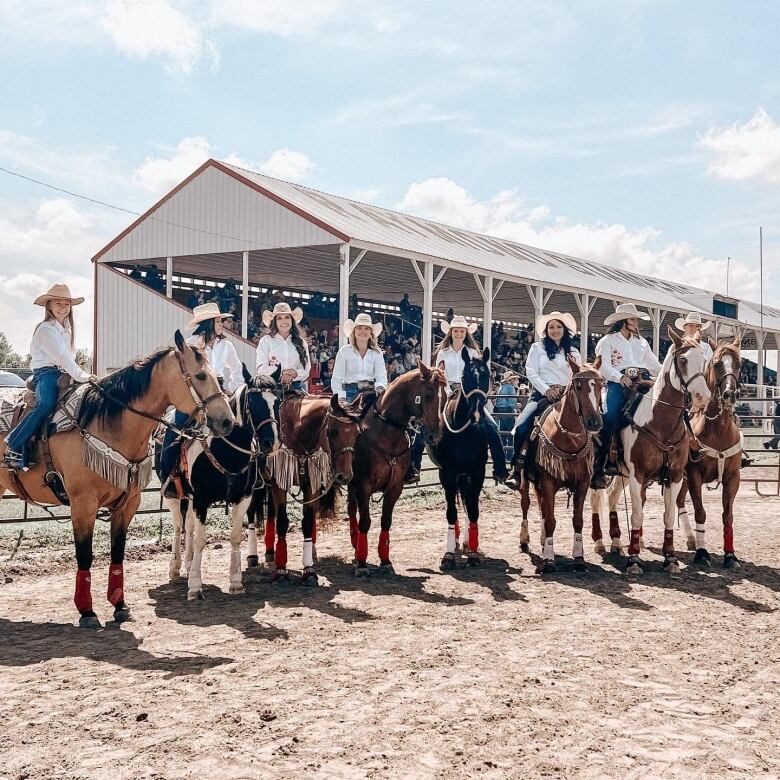 Ten women are on horses in front of a white grandstand. 