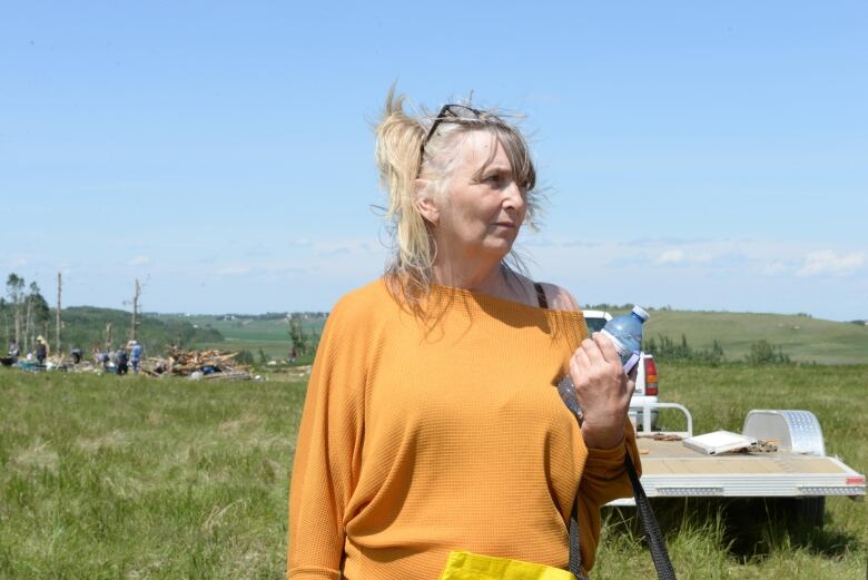 A woman in an orange sweater holds a water bottle. 