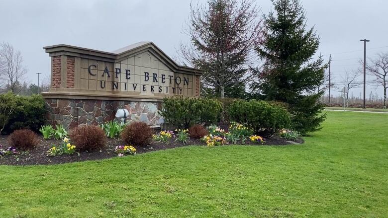 A brick sign surrounded by flowers and shrubs indicates the entrance to Cape Breton University.