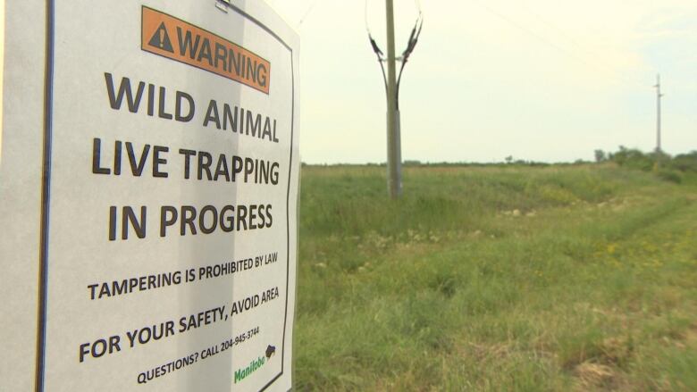 A sign reads 'wild animal live trapping in progress, tampering is prohibited, for your safety avoid the area.'