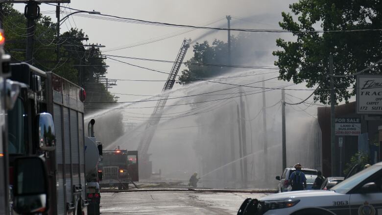 Several fire truck hoses douse water on a complex of industrial buildings on fire.