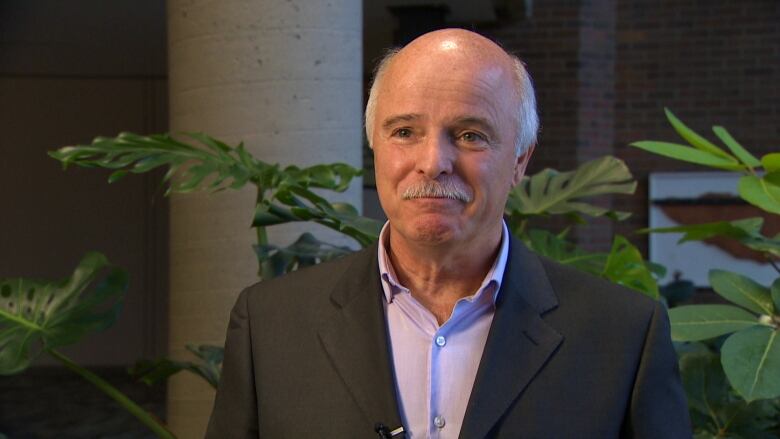 A smiling man wearing a suit in front of some plants.