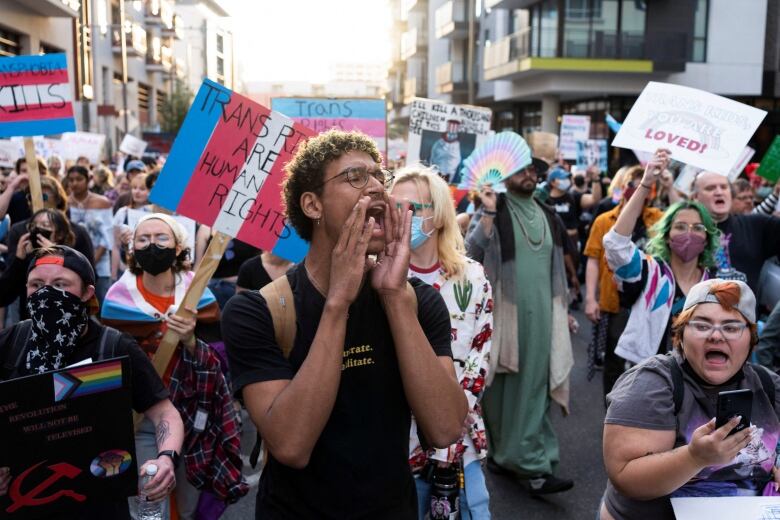 A crowd of people with trans flags and signs that say 'Trans Rights are Human Rights' march in the streets.