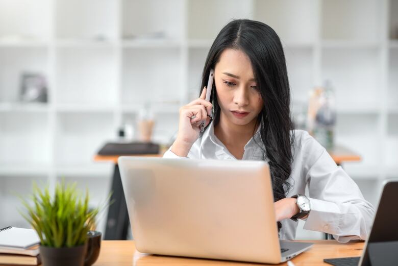 Woman looks down at laptop screen while on handset