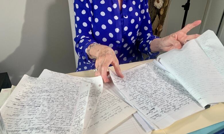 A woman's hands flip through hand-written notes strewn across a kitchen table.