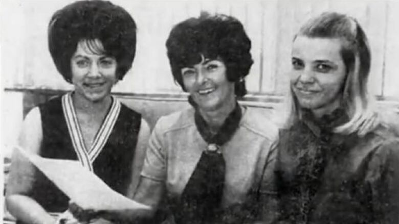 A newspaper clipping showing three women sitting down and smiling at the camera. 