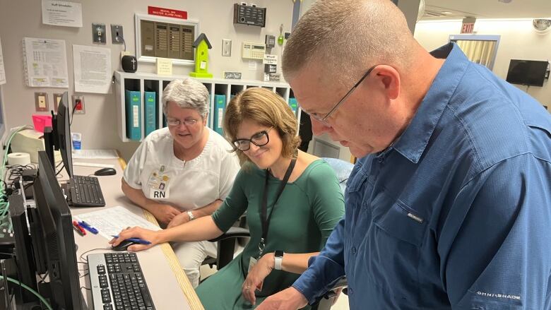 A doctor looks over papers as two staff look on at a rural hospital nursing station. 