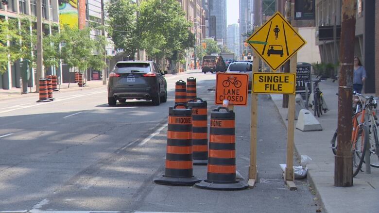 Signage on Adelaide Street in downtown Toronto showing the bike lane closed. A sign showing vehicles and bikes in a single file is next to it.