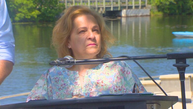 A woman stands behind a podium in front of a waterway.