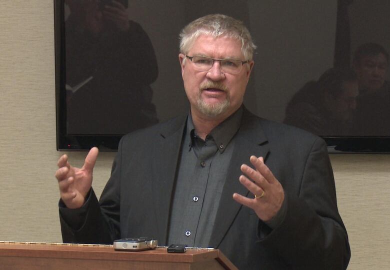 A man in a suit with his hands in front of him as he explains something standing up. 