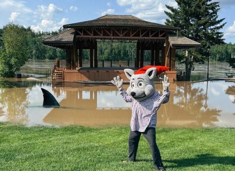 A mascot at the Magnificente River Rats Festival stands beside the overflowing Athabasca River.