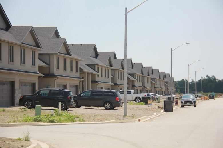 A picture of a sub division in the last steps of being finished. Cars sit in the drive way but no cement has been poured, lawns have not grown in yet.