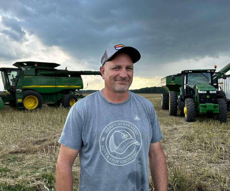 Farmer stands in front of combine, the sky looks ominous as dark clouds roll in. 