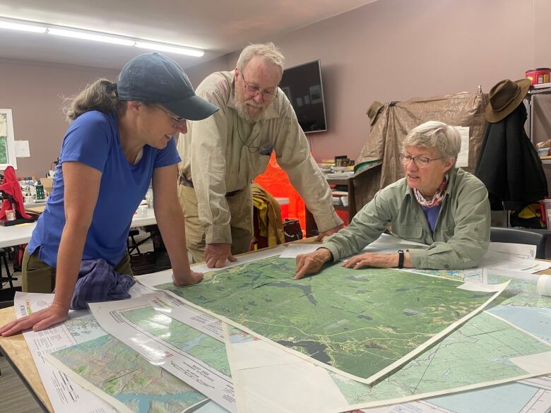 A woman and a man stand over a table where another woman is seated looking at a map.