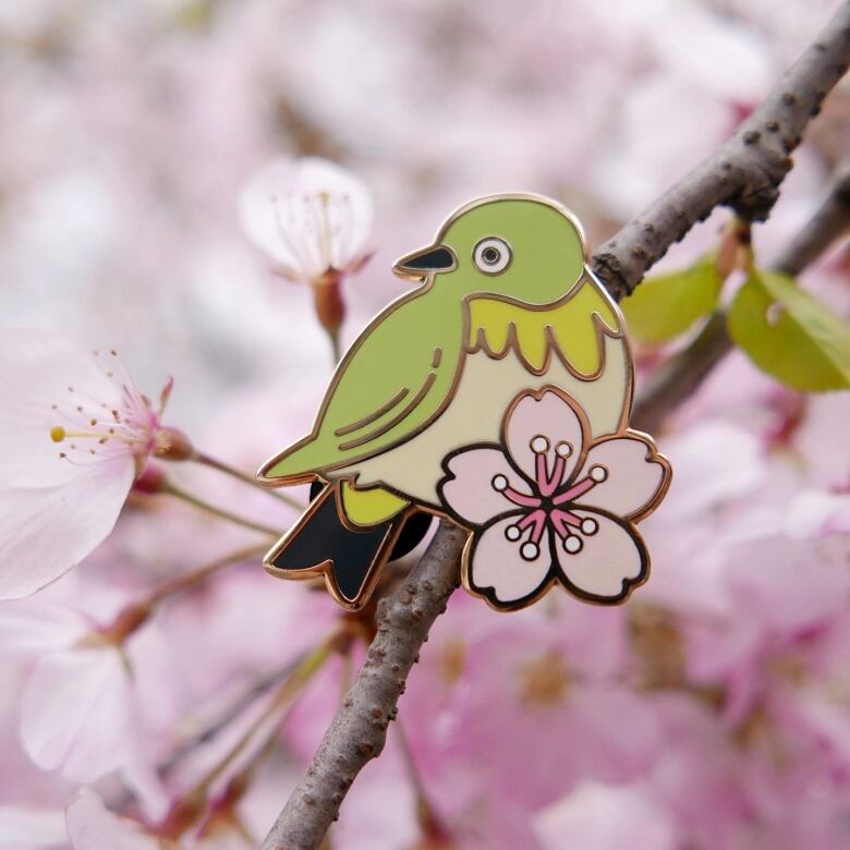 A pin of a green bird against a pink blossoming tree.