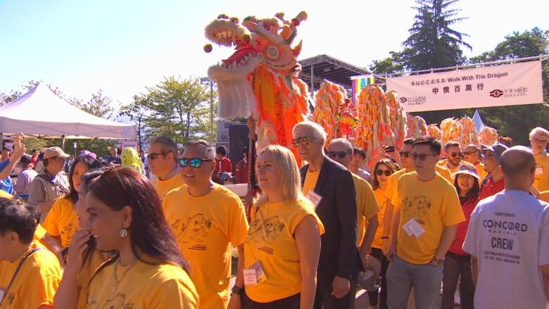 Hundreds of people march along with a Chinese dragon held up by marchgoers on a sunny day.