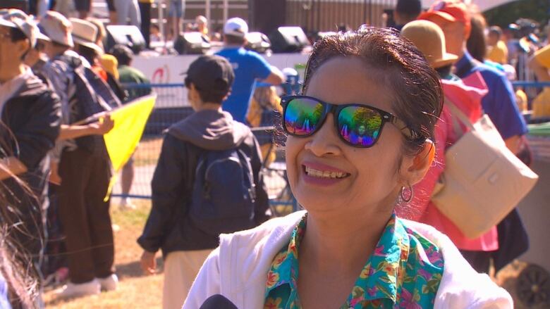 An older East Asian woman smiles while wearing sunglasses outdoors.