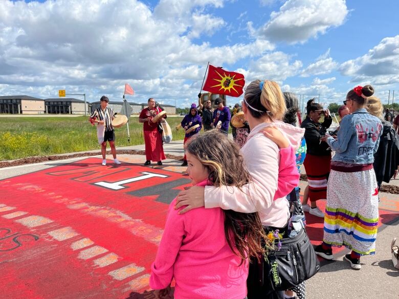 A group of people stand around a painting on the ground of red dress that says 