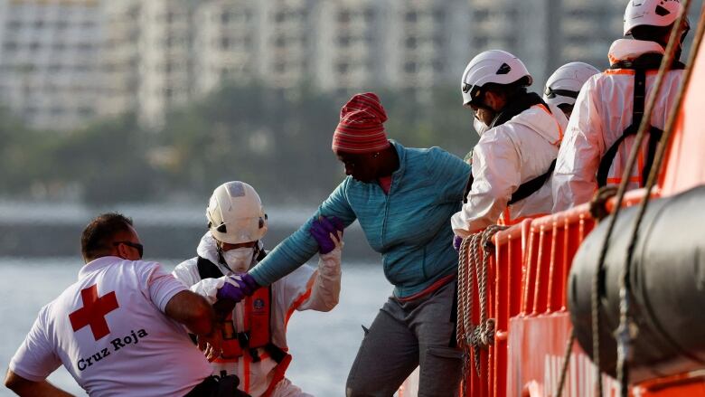 A migrant is helped off a ship by Red Cross and rescue workers.