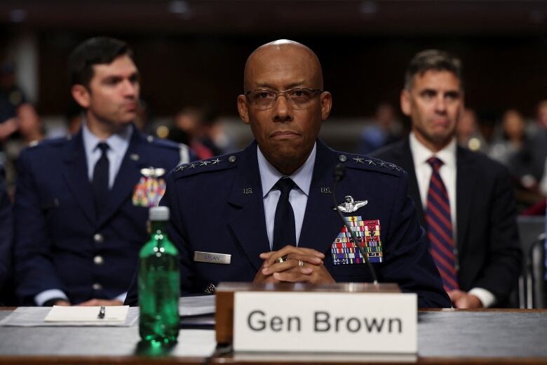 A man in glasses and a military uniform is shown seated at a table.