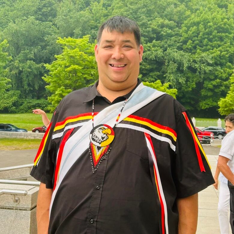 An Indigenous man wears a ribbon shirt and medallion