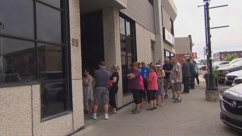 A lineup of people on a sidewalk outside a bank.