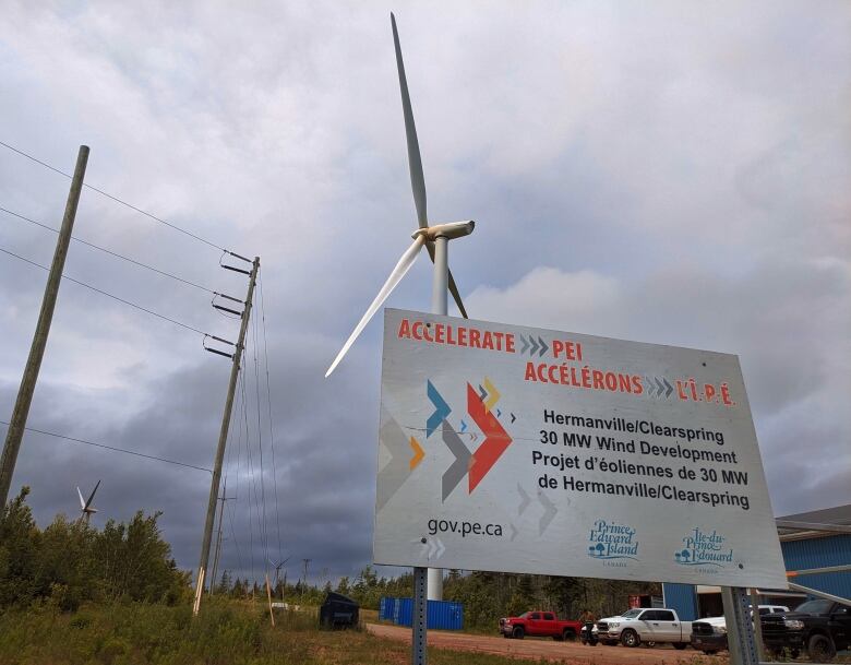 A wind turbine along a dirt road in P.E.I. with a large sign in front of it. 