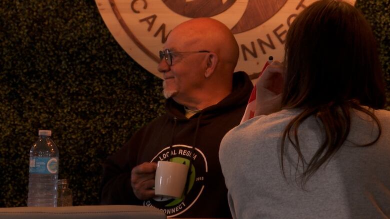 A man sits at a business holding a coffee cup.