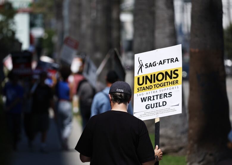 A person facing away from the camera holds a sign that reads, 'Unions Stand Together.'