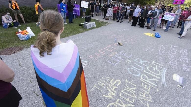 girl with pride flag and chalked messages on the pavement in front of her