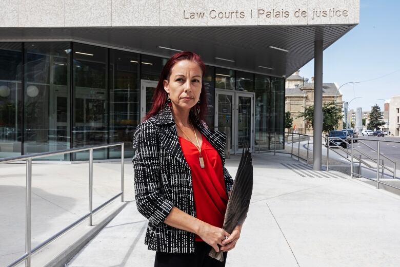 A woman stands in front of the Winnipeg law court building holding an eagle feather 