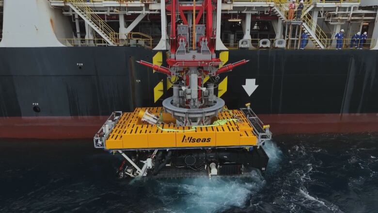 A yellow seabed rover is lowered into the water from a ship.